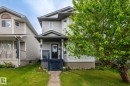 Two-story residence featuring light gray siding, a covered front porch with blue railings, a dark entry door, and a mature tree providing natural shade - 128 Brookview Wy, Stony Plain, AB 