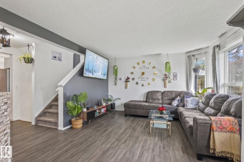 Spacious living area featuring wood-finish flooring, a neutral color palette, and multiple windows allowing natural light - 128 Brookview Wy, Stony Plain, AB 