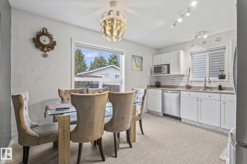 Bright kitchen and dining area featuring white cabinetry, stainless steel appliances, a white brick-look backsplash, and a contemporary light fixture - 128 Brookview Wy, Stony Plain, AB 