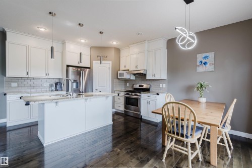 Open-concept kitchen featuring white cabinetry, light-colored countertops, subway tile backsplash, stainless steel appliances, and wood-finish flooring - 21223 58 Avenue, Edmonton, AB 