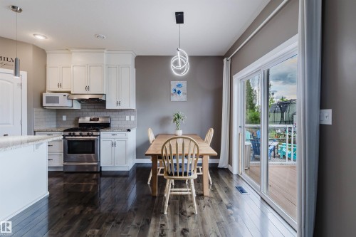 Open-concept kitchen and dining area featuring white cabinetry, stainless steel appliances, a subway tile backsplash, and wood-finish flooring - 21223 58 Avenue, Edmonton, AB 