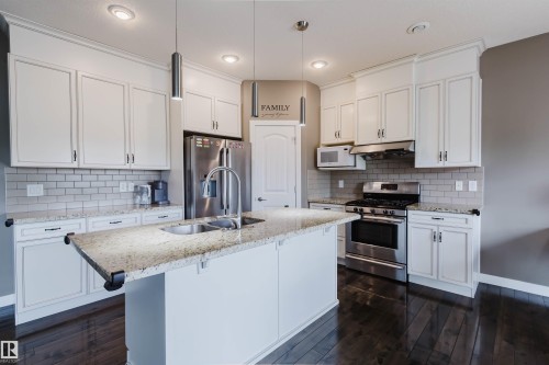 Kitchen featuring a central island with a double basin sink, granite countertops, white cabinetry, and stainless steel appliances, including a refrigerator and range - 21223 58 Avenue, Edmonton, AB 