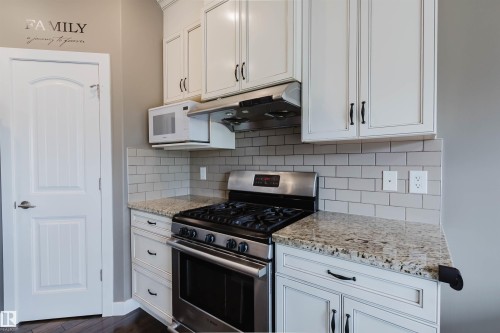 Kitchen featuring a stainless steel range with overhead microwave and ventilation, light-toned cabinetry, granite-finish countertops, and subway tile backsplash - 21223 58 Avenue, Edmonton, AB 