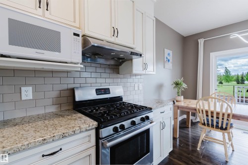 Kitchen featuring light-toned cabinetry with dark hardware, granite-style countertops, a subway tile backsplash, and a stainless steel range with overhead microwave - 21223 58 Avenue, Edmonton, AB 