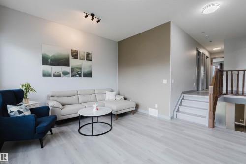 Spacious living area featuring light wood-finish flooring, a contemporary track light fixture, and a neutral color palette - 21223 58 Avenue, Edmonton, AB 