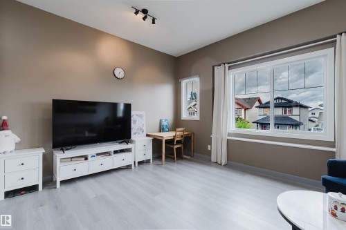 Living area featuring light wood-finish flooring, a large window with white trim, and neutral-toned walls - 21223 58 Avenue, Edmonton, AB 