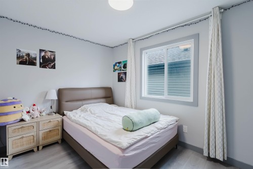 Bright bedroom featuring a large window with white blinds and grey trim, light grey walls, a flush-mount ceiling light, and wood-finish flooring - 21223 58 Avenue, Edmonton, AB 