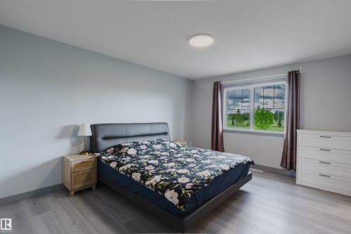 Spacious room featuring wood-finish flooring, light grey wall paint, and a large window with white trim - 21223 58 Avenue, Edmonton, AB 