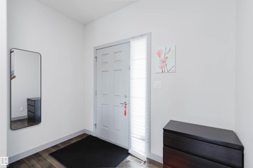 Entryway featuring a paneled door with a sidelight, wood-finish flooring, and light-toned walls - 21223 58 Avenue, Edmonton, AB 