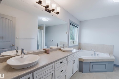 Bathroom featuring a dual vanity with vessel sinks, light-toned countertop, and white cabinetry with dark hardware - 21223 58 Avenue, Edmonton, AB 