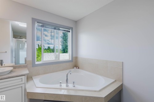 Corner soaking tub with tile surround, large window, double vanity with vessel sinks, and a glass-enclosed shower - 21223 58 Avenue, Edmonton, AB 