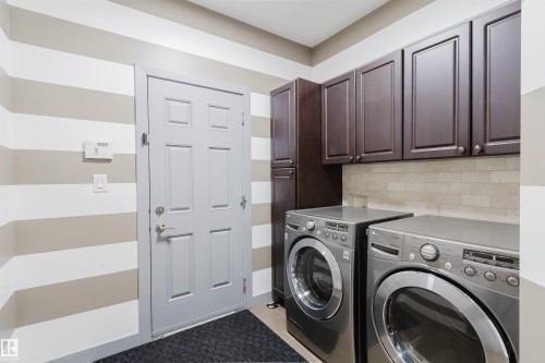 Laundry area featuring dark wood-finish cabinetry, a built-in tall storage cabinet, a light-toned tile backsplash, and a paneled entry door - 21223 58 Avenue, Edmonton, AB 