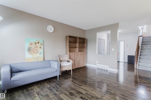Spacious living area featuring rich wood-finish flooring, a neutral wall palette, and a built-in wood-toned storage unit - 21223 58 Avenue, Edmonton, AB 