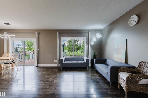 Open-concept living area featuring wood-finish flooring, a contemporary chandelier, and large sliding glass doors opening to an outdoor deck with white railings - 21223 58 Avenue, Edmonton, AB 