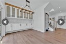 Open-concept interior featuring wood-finish flooring, a long built-in cabinet system with frosted glass uppers, herringbone tile backsplash, and a modern chandelier - 13140 187 Avenue, Edmonton, AB 