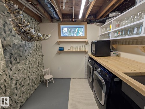 Dedicated laundry area featuring a wood-finish countertop, built-in shelving, two large appliances, and a small window for natural light - 4208 89 Street, Edmonton, AB - Indoor Photo Showing Laundry Room