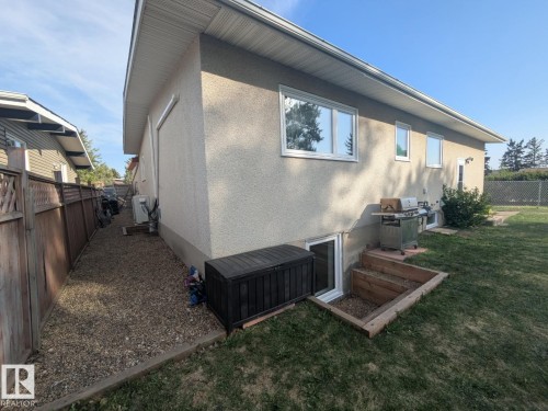 Stucco exterior featuring multiple windows and a basement egress window with a timber-framed well - 4208 89 Street, Edmonton, AB - Outdoor With Exterior