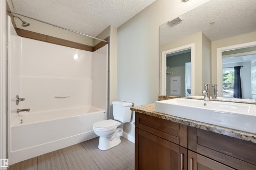 Bathroom featuring a white tub/shower combination, toilet, and a vanity with a rectangular vessel sink - 115 1238 Windermere Way, Edmonton, AB 