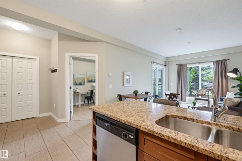 Kitchen island featuring a double basin stainless steel sink with gooseneck faucet and granite-style countertop - 115 1238 Windermere Way, Edmonton, AB 