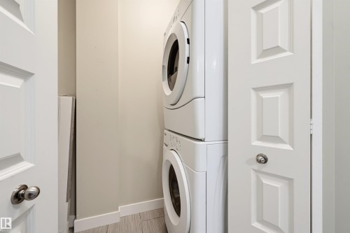 Dedicated laundry area featuring a stacked washer and dryer, white paneled doors with chrome hardware, and light-toned flooring - 115 1238 Windermere Way, Edmonton, AB 