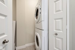 Dedicated laundry area featuring a stacked washer and dryer, white paneled doors with chrome hardware, and light-toned flooring - 