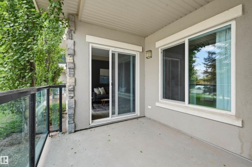 Private patio space featuring a concrete surface, glass and metal railings, and a stucco exterior with stone accents - 115 1238 Windermere Way, Edmonton, AB 