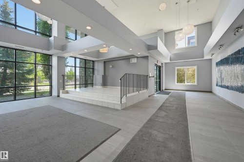 Spacious entryway featuring floor-to-ceiling windows, multi-level flooring, recessed lighting, contemporary pendant lights, and a decorative wall art piece - 115 1238 Windermere Way, Edmonton, AB 