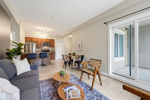 Open-concept living area featuring light wood-finish flooring, a kitchen with wood cabinetry and stainless steel appliances, a dining area, and sliding glass patio doors - 115 1238 Windermere Way, Edmonton, AB 
