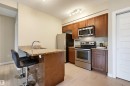 Modern kitchen featuring stainless steel appliances, granite countertops, wood cabinetry, and a peninsula with a built-in sink - 115 1238 Windermere Way, Edmonton, AB 