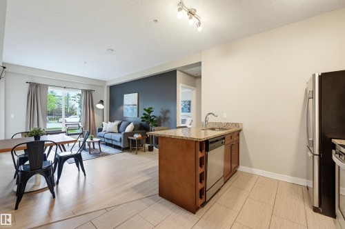 Kitchen island with granite countertop and integrated sink, stainless steel dishwasher, and built-in wine rack - 115 1238 Windermere Way, Edmonton, AB 