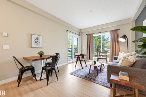 Open-concept living space featuring wood-finish flooring, a neutral color palette, and abundant natural light from the large windows - 115 1238 Windermere Way, Edmonton, AB 