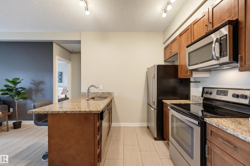 Kitchen featuring wood cabinetry, stainless steel appliances, granite countertops, and tiled flooring - 115 1238 Windermere Way, Edmonton, AB 