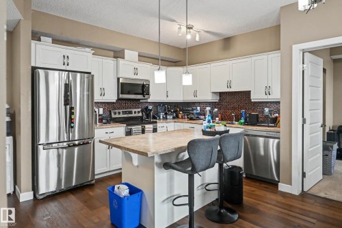 Kitchen featuring white cabinetry, stainless steel appliances, a center island with countertop seating, wood-finish flooring, and a mosaic tile backsplash - 402 8730 82 Avenue, Edmonton, AB 
