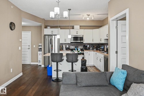 Modern kitchen featuring white cabinetry, stainless steel appliances, a breakfast bar, dark wood-finish flooring, and pendant lighting - 402 8730 82 Avenue, Edmonton, AB 