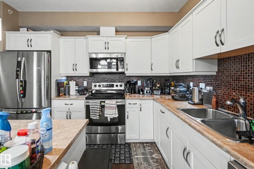 Kitchen featuring white cabinetry with silver hardware, stainless steel appliances, a mosaic tile backsplash, and light-toned countertops - 402 8730 82 Avenue, Edmonton, AB 