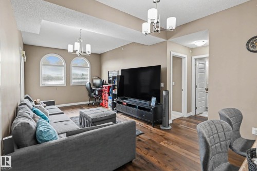 Living area featuring wood-finish flooring, two arched windows with blinds, recessed ceiling accents, and two contemporary light fixtures - 402 8730 82 Avenue, Edmonton, AB 