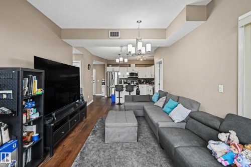 Open-concept living area with wood-finish flooring extending into the kitchen - 402 8730 82 Avenue, Edmonton, AB 