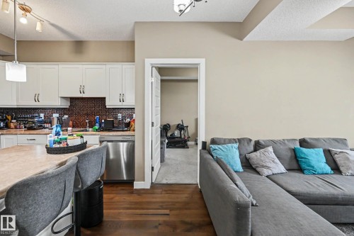 Open-concept living area featuring rich wood-finish flooring, a contemporary kitchen with white cabinetry and a patterned backsplash, and a built-in breakfast bar - 402 8730 82 Avenue, Edmonton, AB 