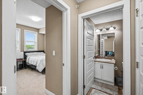 Hallway featuring a bedroom entry with carpet flooring and dual windows, and a bathroom entry with a white vanity, a rectangular sink, and a three-light fixture - 402 8730 82 Avenue, Edmonton, AB 