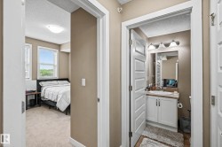 Hallway featuring a bedroom entry with carpet flooring and dual windows, and a bathroom entry with a white vanity, a rectangular sink, and a three-light fixture - 