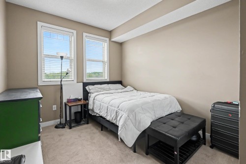 Neutral-toned interior room featuring two windows with white blinds, light beige wall paint, and wall-to-wall carpeting - 402 8730 82 Avenue, Edmonton, AB 