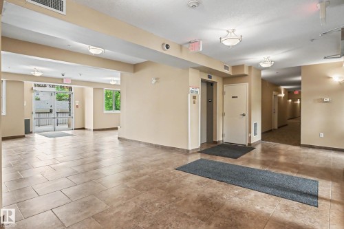 Spacious lobby featuring large format tile flooring, multiple flush-mount ceiling lights, light beige wall paint, and an elevator access point - 402 8730 82 Avenue, Edmonton, AB 