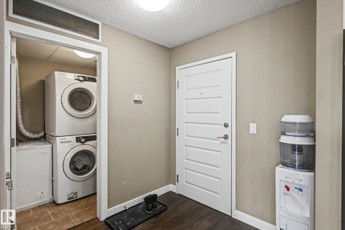 Dedicated laundry area with stacked washer and dryer, adjacent to an entry door with five horizontal panels - 402 8730 82 Avenue, Edmonton, AB 