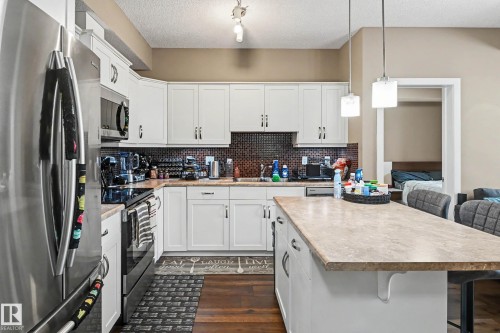 Modern kitchen featuring white cabinetry, a large center island, dark wood-finish flooring, and stainless steel appliances - 402 8730 82 Avenue, Edmonton, AB 