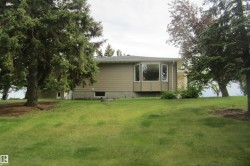 Exterior showcasing a bay window, tan siding, and a sloped lawn with mature trees - 