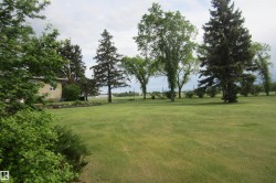 Expansive green lawn with mature trees and a partial view of a single-story residence featuring light-colored siding - 