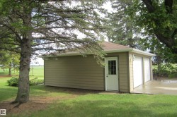 Detached two-car garage featuring tan horizontal siding, a brown shingle roof, and white garage doors - 