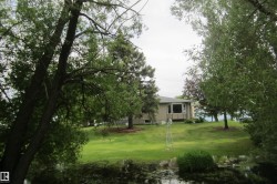 Sloped green lawn descending to a pond with a detached single-story residence featuring a bay window - 