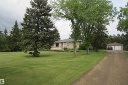 Expansive lawn featuring mature trees and a gravel driveway leading to a detached two-car garage - 