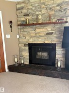 Stone-clad fireplace featuring a dark metal firebox screen and a floating wood mantel - 
